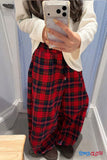 Person wearing red plaid pants and a white sweater, taking a mirror selfie.