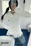 Person wearing a white sweater with star patterns and fringes, sitting indoors.