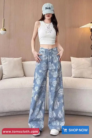 Woman wearing a white top and blue floral pants in a living room setting with 'Toms Cloth' branding.
