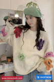 Person wearing a white sweater with colorful flower patterns, taking a mirror selfie.