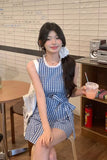 Woman in a blue checkered dress holding a drink in a casual indoor setting.
