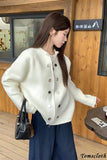 Woman in a white coat with black buttons standing indoors against a wooden wall.