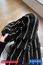 Black textured fabric with gold accents held by a hand on a wooden floor.