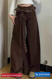 Brown wide-leg pants with a plaid belt worn by a person, with 'tomscloth.com' branding at the bottom.