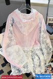 Pink lace top with sheer overlay on a hanger against a blurred indoor background.