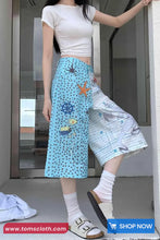 Person wearing a white top and blue skirt with starfish design, standing indoors.