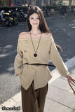 Woman in beige off-shoulder top and brown pants standing on a street.
