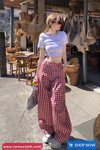 Woman in a casual outfit with plaid pants and a white top, standing in an outdoor setting with wicker baskets and tables.