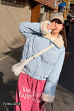 Person wearing a light blue puffer jacket with fur trim and pink pants with text, standing on a street.
