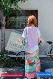 Woman holding a colorful bag with a bicycle and 'La Perla' sign in the background