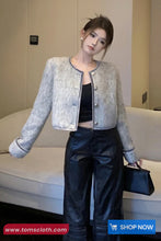 Woman wearing a light gray textured jacket over a black top and pants, holding a black handbag.
