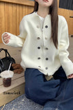 Person wearing a white cardigan with black buttons, sitting on a wooden bench.