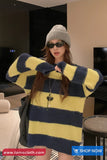 Woman wearing a yellow and blue striped sweater with sunglasses indoors.