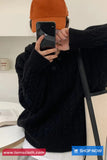 Person wearing a black cable knit sweater and orange cap taking a mirror selfie.