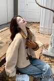 Woman wearing a beige jacket with brown accents sitting on a wooden bench.