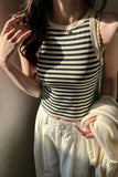 Person wearing a black and white striped tank top and white pants, holding a beige sweater.