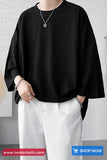 Person wearing a black oversized shirt and white pants with a gray background
