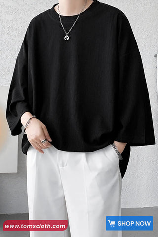 Person wearing a black oversized shirt and white pants with a gray background