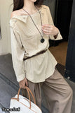 Woman wearing a beige off-shoulder top and beige pants, holding a white bag.