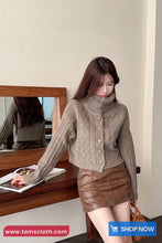 Woman wearing a brown sweater and leather skirt in front of a mirror, with a 'Shop Now' button visible.