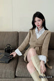 Woman sitting on a couch wearing a beige sweater dress with a white shirt underneath.