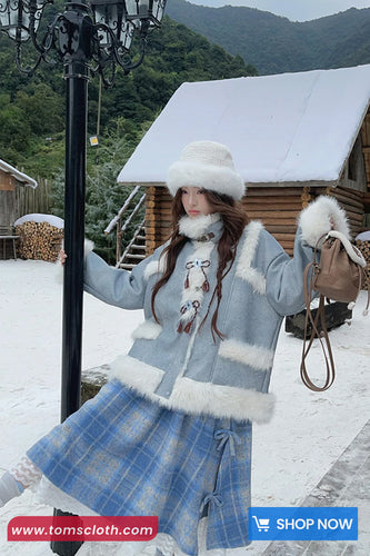Woman in winter clothing with a snowy background and wooden cabin.