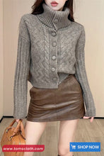 Woman wearing a gray knitted cardigan over a brown leather skirt with a beige background.