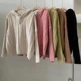 Row of colorful cable knit sweaters hanging on a rack against a neutral background