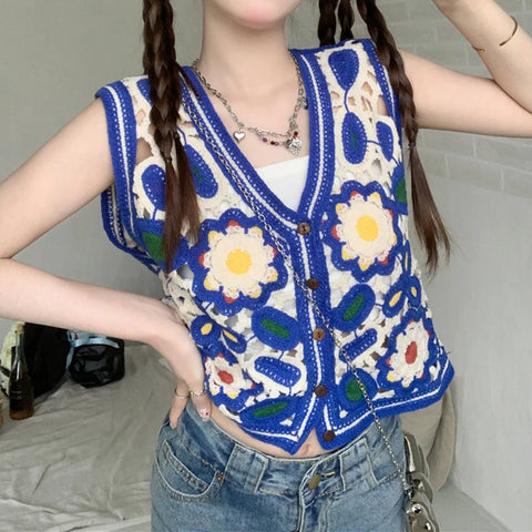 Person wearing a colorful floral crochet vest over a white shirt and blue jeans.