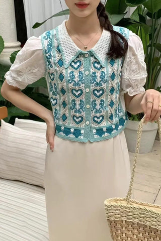 Person wearing a light blue cardigan with colorful designs, standing in front of a rack with other cardigans.