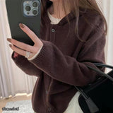 Person wearing a brown cardigan holding a phone with a blurred background